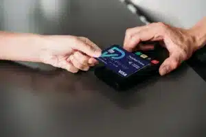 A person holds a credit card near a card reader for a contactless payment, while another person holds the device on a gray counter.